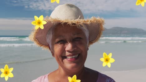 Zusammengesetztes-Video-Von-Blumensymbolen,-Die-Auf-Eine-Afroamerikanische-ältere-Frau-Fallen,-Die-Am-Strand-Lächelt