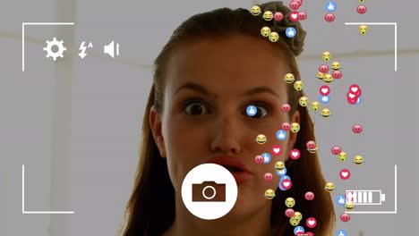 Camera-interface-over-multiple-face-emojis-and-icons-against-caucasian-woman-making-funny-faces
