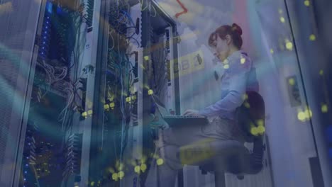 Animation-of-server-room-over-caucasian-female-worker-inspecting-and-using-laptop-in-server-room