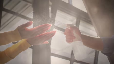 Video-of-light-over-diverse-colleagues-disinfecting-hands-at-work