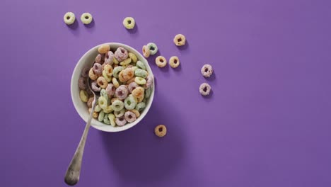 Video-of-colorful-breakfast-cereals-with-bowl-and-spoon-on-purple-background