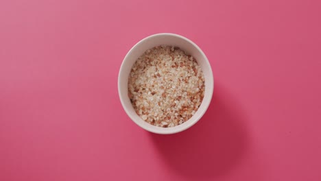 Video-of-high-angle-view-of-bowl-of-organic-salt-on-pink-background