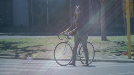 Animation-of-shapes-moving-over-biracial-woman-with-face-mask-walking-with-bicycle