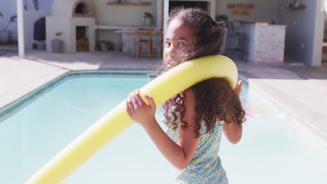 Portrait-of-happy-biracial-girl-looking-at-camera-at-swimming-pool
