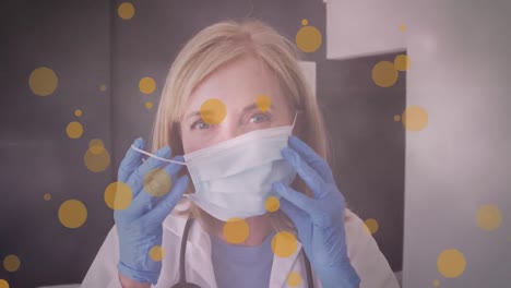 Animation-of-yellow-spots-over-female-caucasian-doctor-putting-face-mask-on
