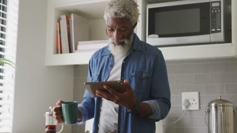 Video-Eines-Glücklichen-Afroamerikanischen-älteren-Mannes,-Der-Kaffee-Trinkt-Und-Ein-Tablet-Benutzt