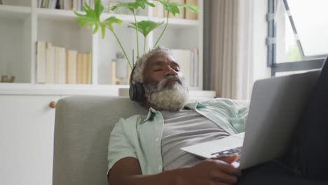 Video-of-african-american-senior-man-using-laptop-and-headphones