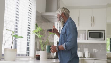 Video-Eines-Afroamerikanischen-älteren-Mannes,-Der-Kaffee-Trinkt-Und-Sein-Smartphone-Benutzt