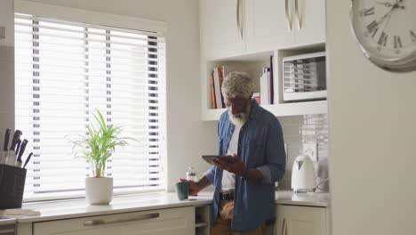 Video-Eines-Afroamerikanischen-älteren-Mannes,-Der-Kaffee-Trinkt-Und-Ein-Tablet-Benutzt