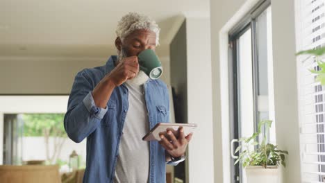 Video-of-african-american-senior-man-drinking-coffee-and-using-tablet