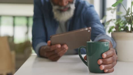 Video-Eines-Afroamerikanischen-älteren-Mannes,-Der-Kaffee-Trinkt-Und-Ein-Tablet-Benutzt