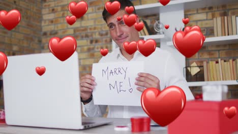 Animation-of-red-hearts-flying-over-caucasian-man-proposing-on-laptop-video-call