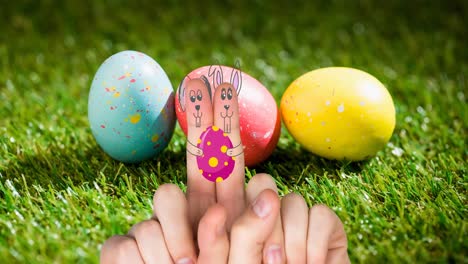 Animation-of-hands-with-drawings-of-rabbit-with-easter-egg-over-easter-eggs-on-grass