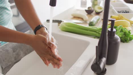 Midsection-of-african-american-woman-washing-hands-in-sink-in-kitchen