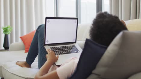 Happy-african-american-woman-sitting-on-sofa,-using-laptop-with-copy-space