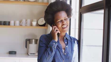 Happy-african-american-woman-talking-on-smartphone-in-kitchen