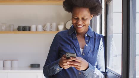 Happy-african-american-woman-using-smartphone-in-kitchen