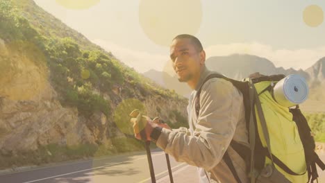 Animation-of-light-spots-over-biracial-man-walking-in-mountains