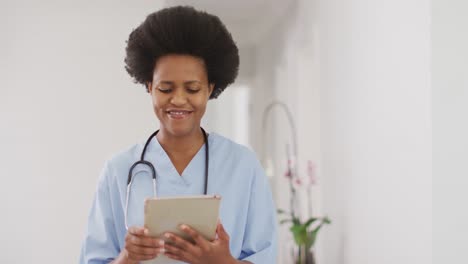 Portrait-of-happy-african-american-female-doctor-using-tablet,-looking-at-camera-and-smiling