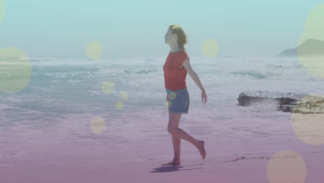 Animation-Von-Lichtflecken-über-Einer-Kaukasischen-Frau,-Die-Am-Strand-Spaziert