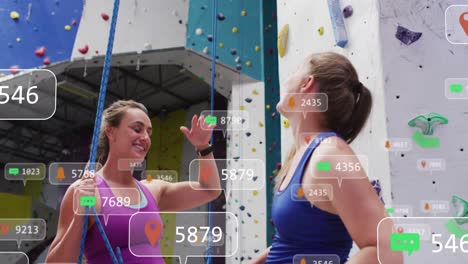 Animation-of-media-icons-over-happy-two-caucasian-women-high-fiving-on-climbing-wall