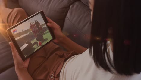 Animation-of-glowing-lights-over-biracial-woman-watching-football-on-tablet