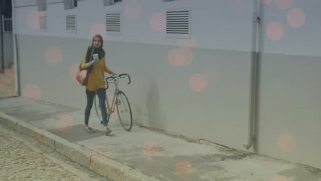 Animation-of-light-spots-over-biracial-woman-walking-with-bike