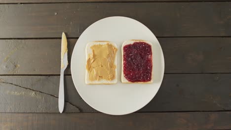 Close-up-view-of-peanut-butter-and-jelly-sandwich-in-a-plate-with-butter-knife-on-wooden-surface
