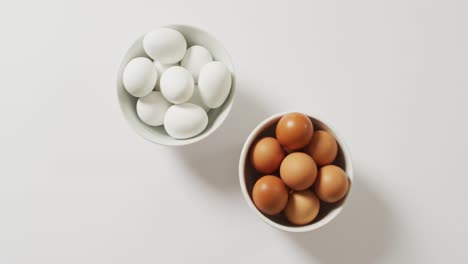 Close-up-of-two-bowls-full-of-brown-and-white-eggs-with-copy-space-on-white-surface