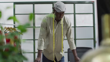 Portrait-of-happy-african-american-male-fashion-designer-wearing-tape-measure-at-office