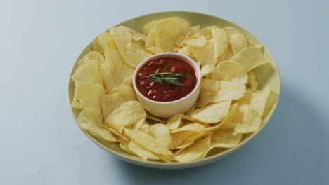 Close-up-of-potato-chips-in-a-bowl-with-sauce-on-blue-surface
