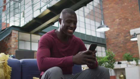 Glücklicher-Afroamerikanischer-Geschäftsmann,-Der-Im-Büro-Sein-Smartphone-Nutzt