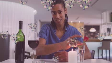 Animation-of-heart-icons-over-happy-biracial-man-with-wine-having-video-call