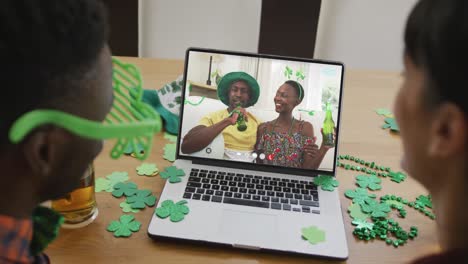 Lächelndes-Afroamerikanisches-Paar-Mit-Bier-Und-Kleeblattförmigen-Gegenständen-Bei-Einem-Videoanruf-Auf-Dem-Laptop