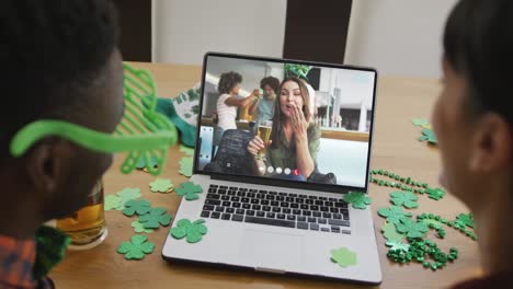 Smiling-caucasian-woman-with-beer-wearing-clover-shape-band-on-video-call-on-laptop