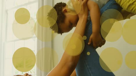 Animation-Von-Gelben-Flecken-über-Einem-Biracial-Vater,-Der-Mit-Seinem-Baby-Spielt