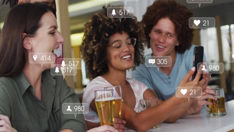 Animation-of-media-icons-over-happy-diverse-friends-using-smartphone-with-beer