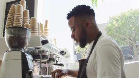 Glücklicher-Afroamerikanischer-Männlicher-Barista,-Der-Im-Café-Kaffee-Mit-Der-Kaffeemaschine-Zubereitet