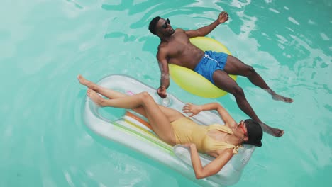 Happy-diverse-couple-wearing-swimming-suits-with-inflatables-at-swimming-pool-in-garden