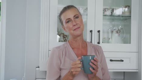Ältere-Kaukasische-Frau-Trägt-Rosa-Hemd-Und-Hält-Eine-Tasse-Kaffee-In-Der-Küche