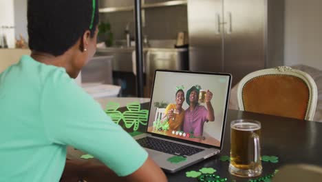 Lächelnde-Afroamerikanische-Männliche-Freunde-Mit-Bier-Und-Kleeblattförmigen-Gegenständen-Bei-Einem-Videoanruf-Auf-Dem-Laptop