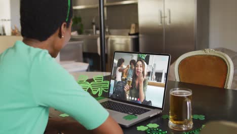 Smiling-caucasian-woman-with-beer-wearing-clover-shape-band-on-video-call-on-laptop