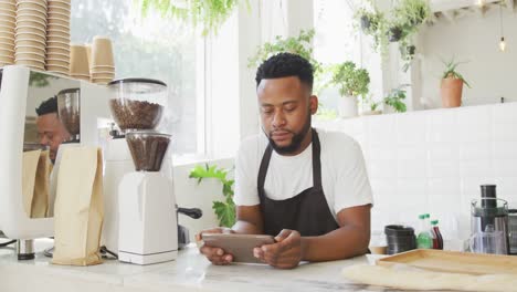 African-american-male-cafe-owner-standing-by-counter-using-tablet-at-cafe