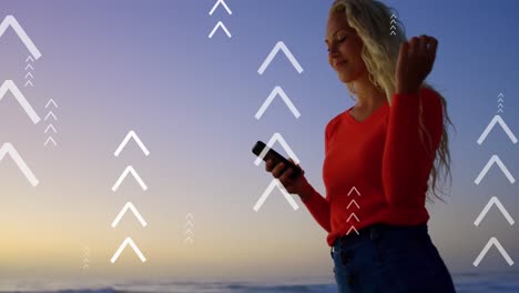 Animation-of-arrows-over-happy-caucasian-woman-using-smartphone-at-sunset