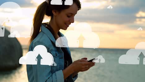 Animation-Von-Wolken-über-Dem-Mittelteil-Einer-Gemischtrassigen-Frau,-Die-Am-Strand-Ihr-Smartphone-Benutzt