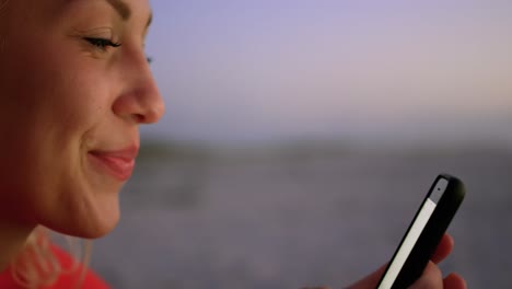 Animation-of-emoticons-over-profile-of-happy-biracial-woman-using-smartphone-at-beach
