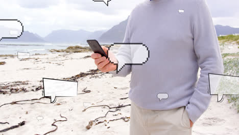 Animation-of-speech-bubbles-over-midsection-of-caucasian-man-using-smartphone-at-beach