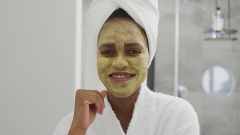 Porträt-Einer-Glücklichen-Afroamerikanischen-Frau-Mit-Schönheitsmaske-Im-Gesicht,-Die-Im-Badezimmer-Lächelt