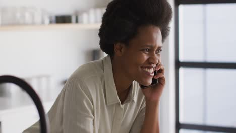 Glückliche-Afroamerikanische-Frau,-Die-Kaffee-Trinkt-Und-In-Der-Küche-Auf-Dem-Smartphone-Spricht