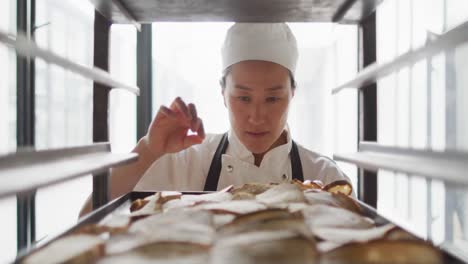 Animation-of-happy-asian-female-baker-checking-freshly-prepared-rolls